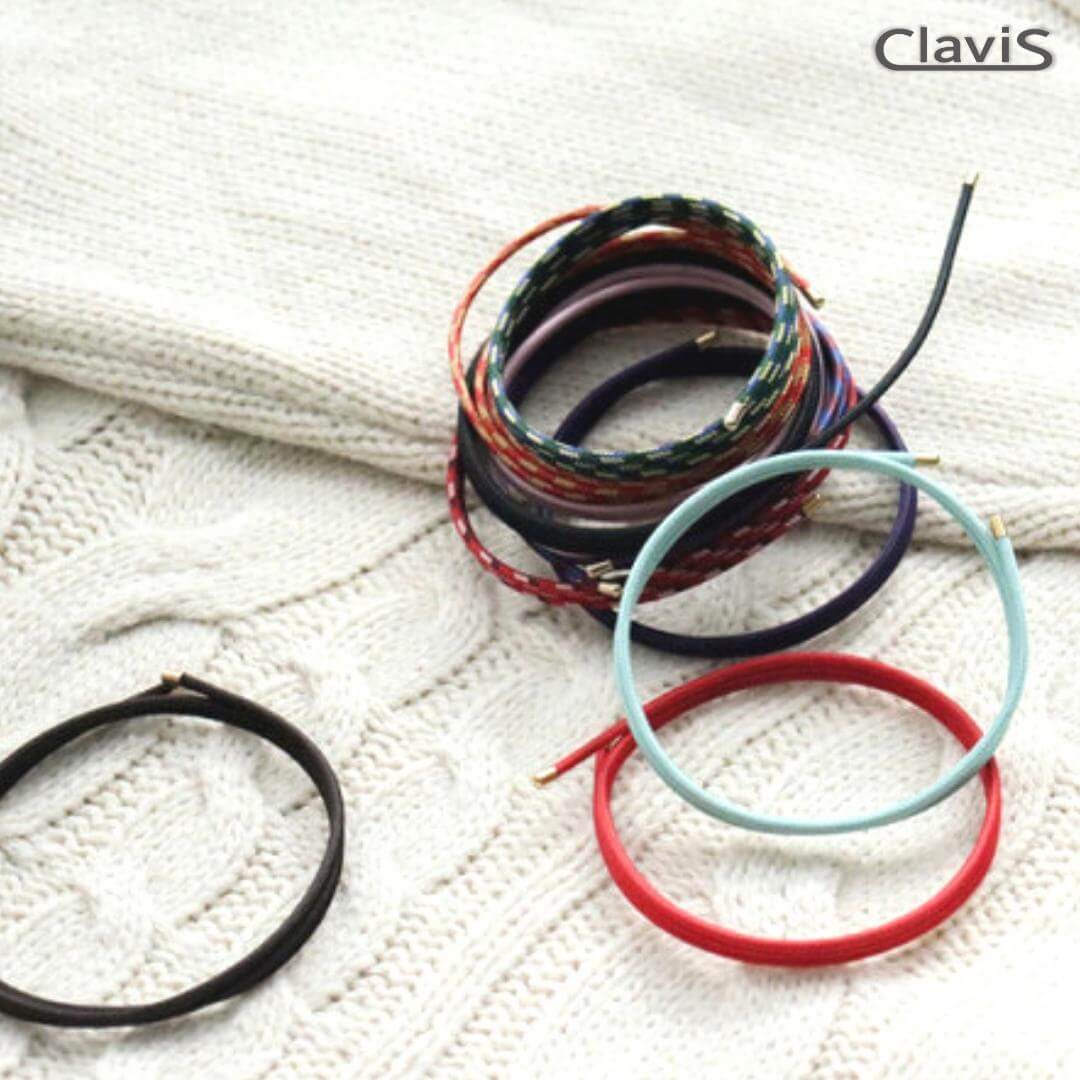 Stack of colorful Clavis magnetic therapy bands on knitted fabric, includes golf, sport performance, and energy bracelets.