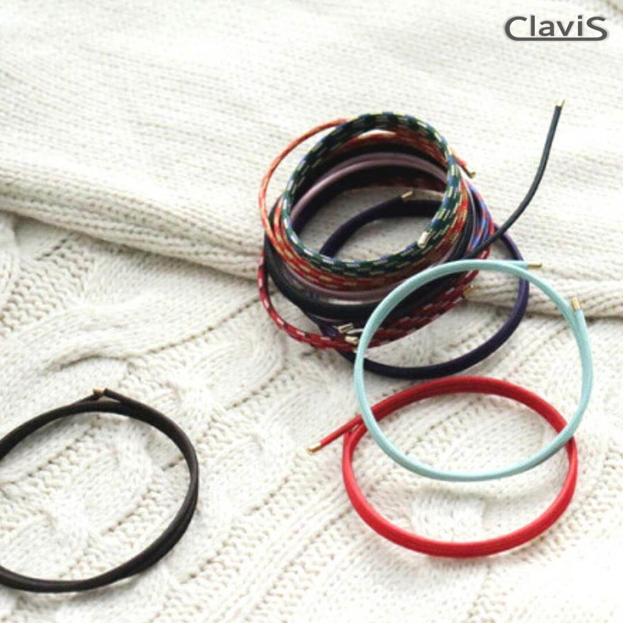 Stack of colorful Clavis magnetic therapy bands on knitted fabric, includes golf, sport performance, and energy bracelets.