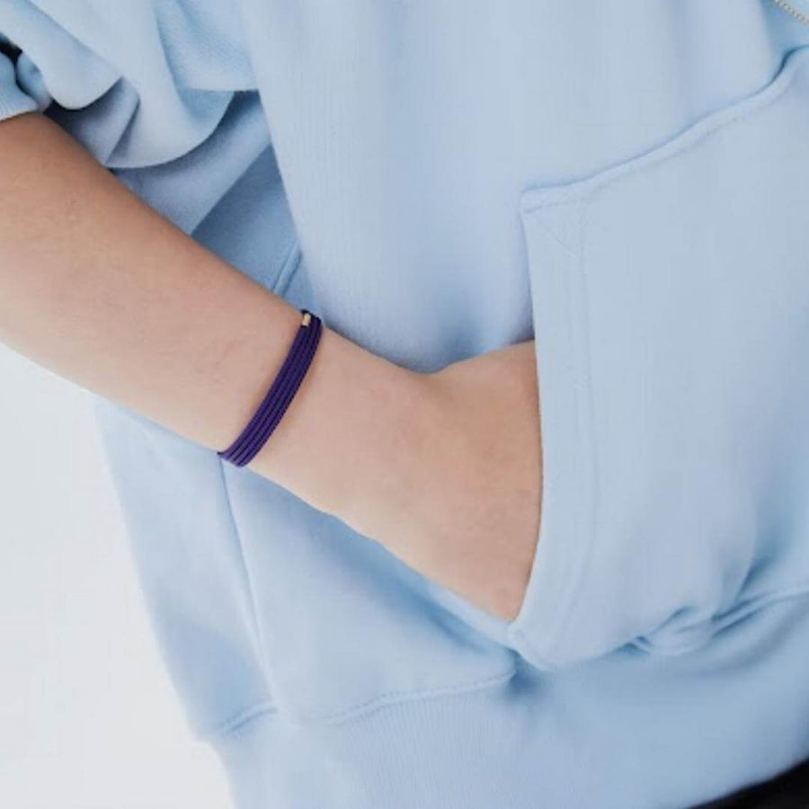 Person wearing a purple layered bracelet with hand in pocket, showcasing a trendy accessory.